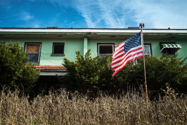 ripped up american flag blowing in the wind in front of abandoned homes